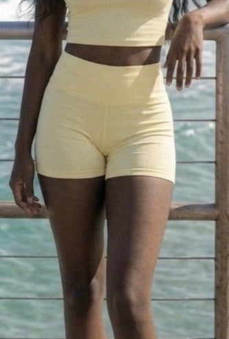 Woman in a yellow ÁMBER Del Mar set standing on a wooden pier by the ocean.