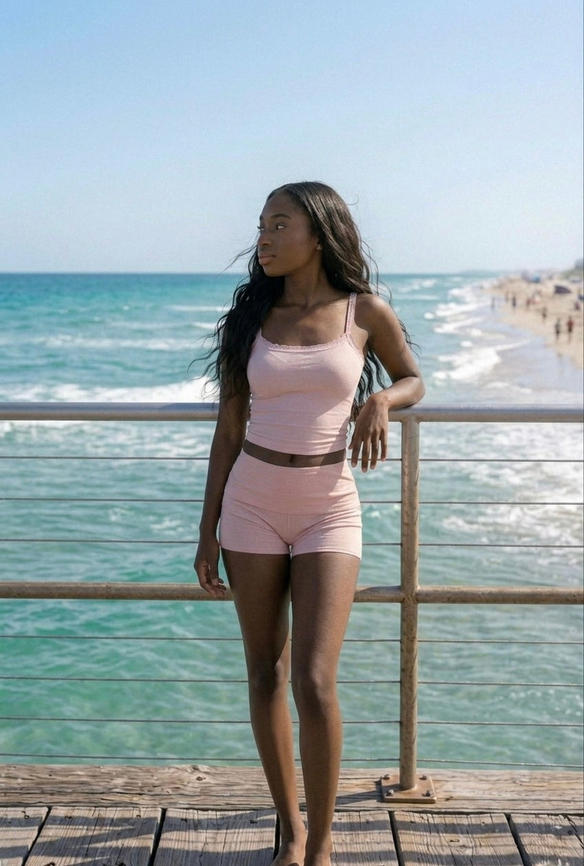 Woman in a pink amber Del Mar outfit standing on a wooden pier by the ocean.