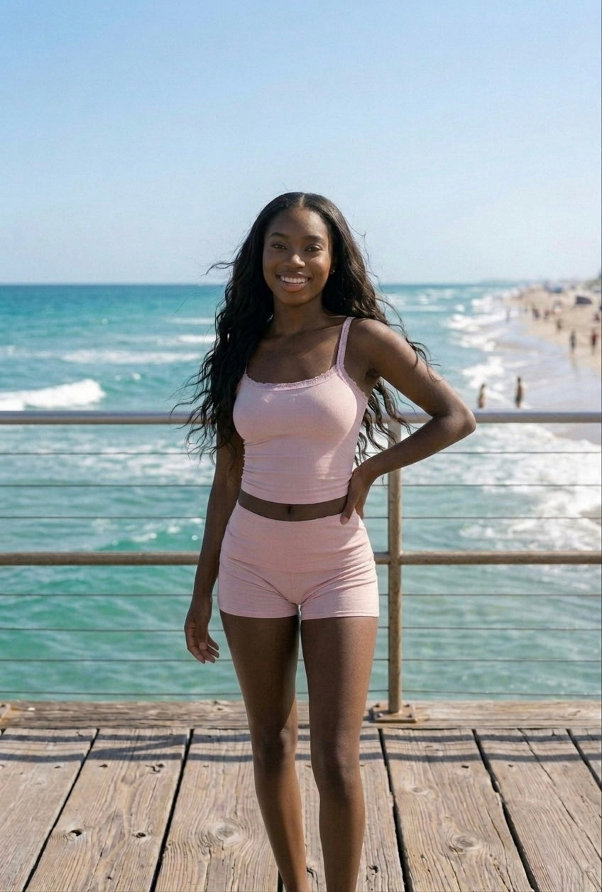 Woman in pink amber Del Mar summer lounge cami standing on a wooden deck by the ocean.
