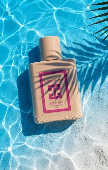 Pretty Girl Eau de Parfum by ÁMBER DEL MAR summer fragrance bottle resting in crystal clear pool water with tropical palm leaf shadows.
