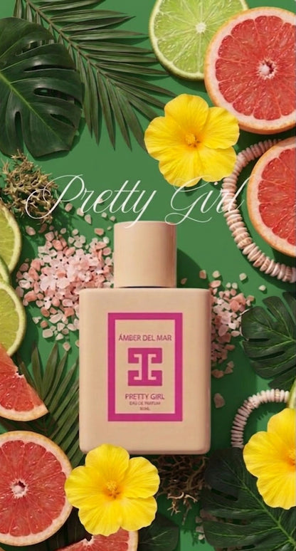 A bottle of Pretty Girl perfume by Amber Del Mar, featuring a pink bottle and pink label, surrounded by tropical fruits, flowers, and leaves on a green background.
