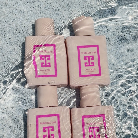 A video showing four AMBER DEL MAR perfume bottles in crystal clear water. Water continuously flows over them, with the sunlight hitting them and highlighting a minimalist pink bottles.